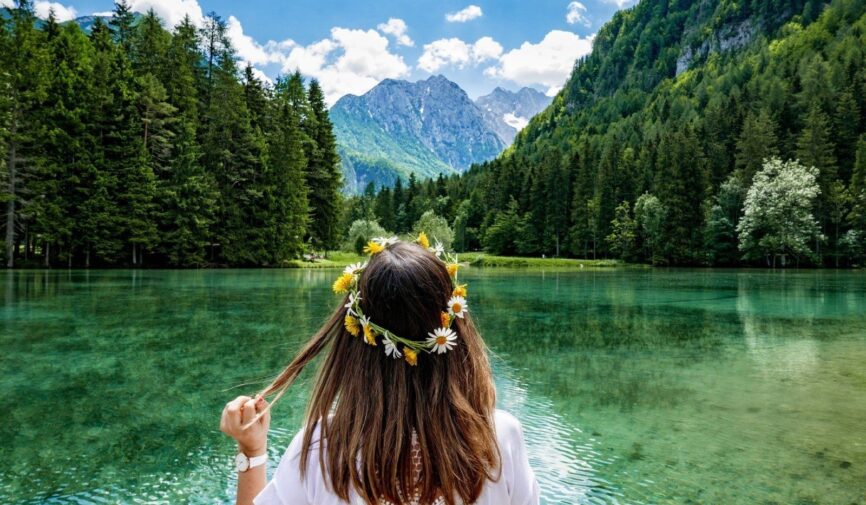 woman-from-behind-woman-in-a-white-top-with-flowers-in-her-hair-sitting-by-a-green-lake-surrounded-by_t20_AV0ZZP-min